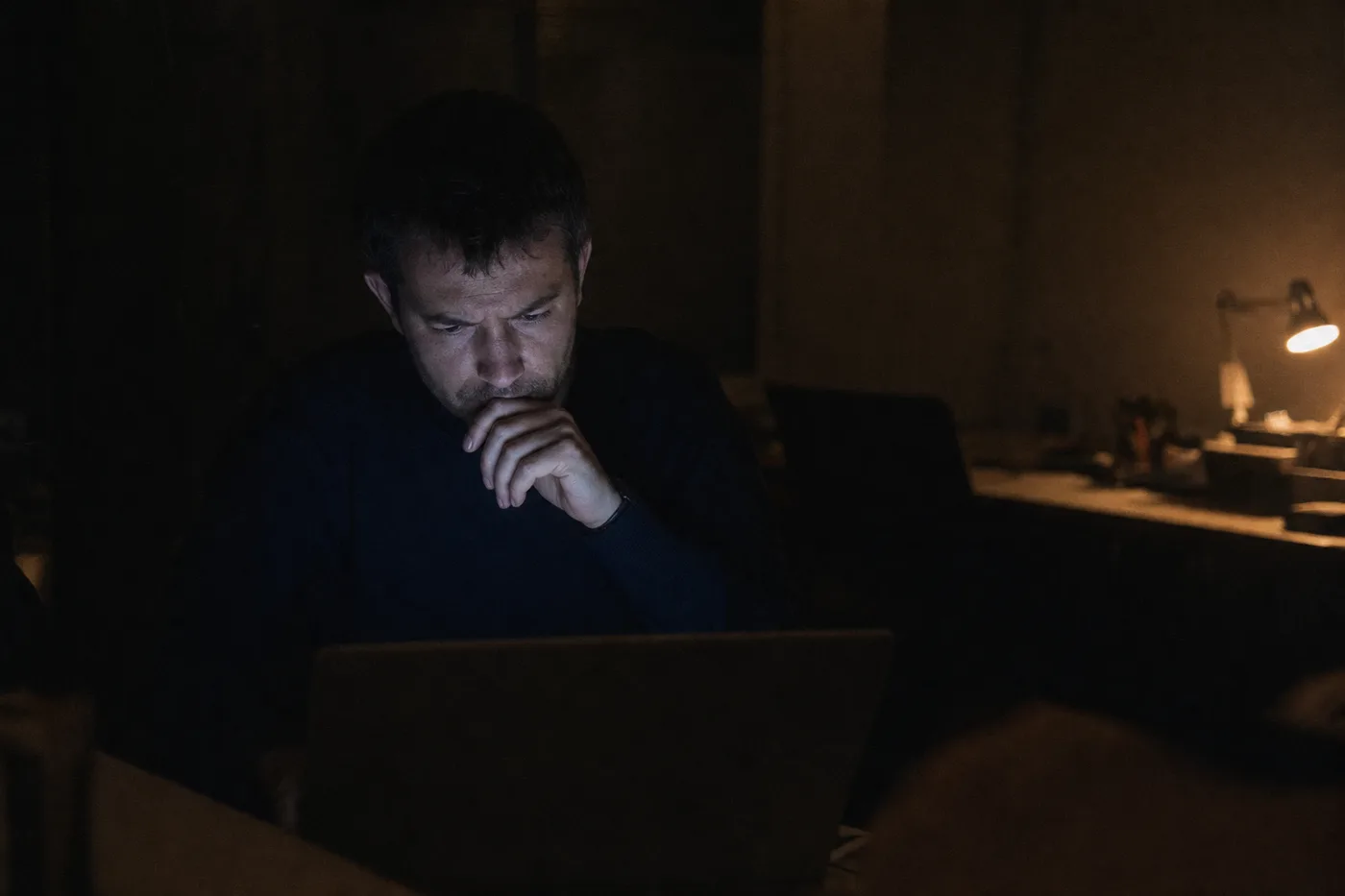 A single employee working late alone at a desk lit only by a laptop, trying to teach themselves new software with no one to help