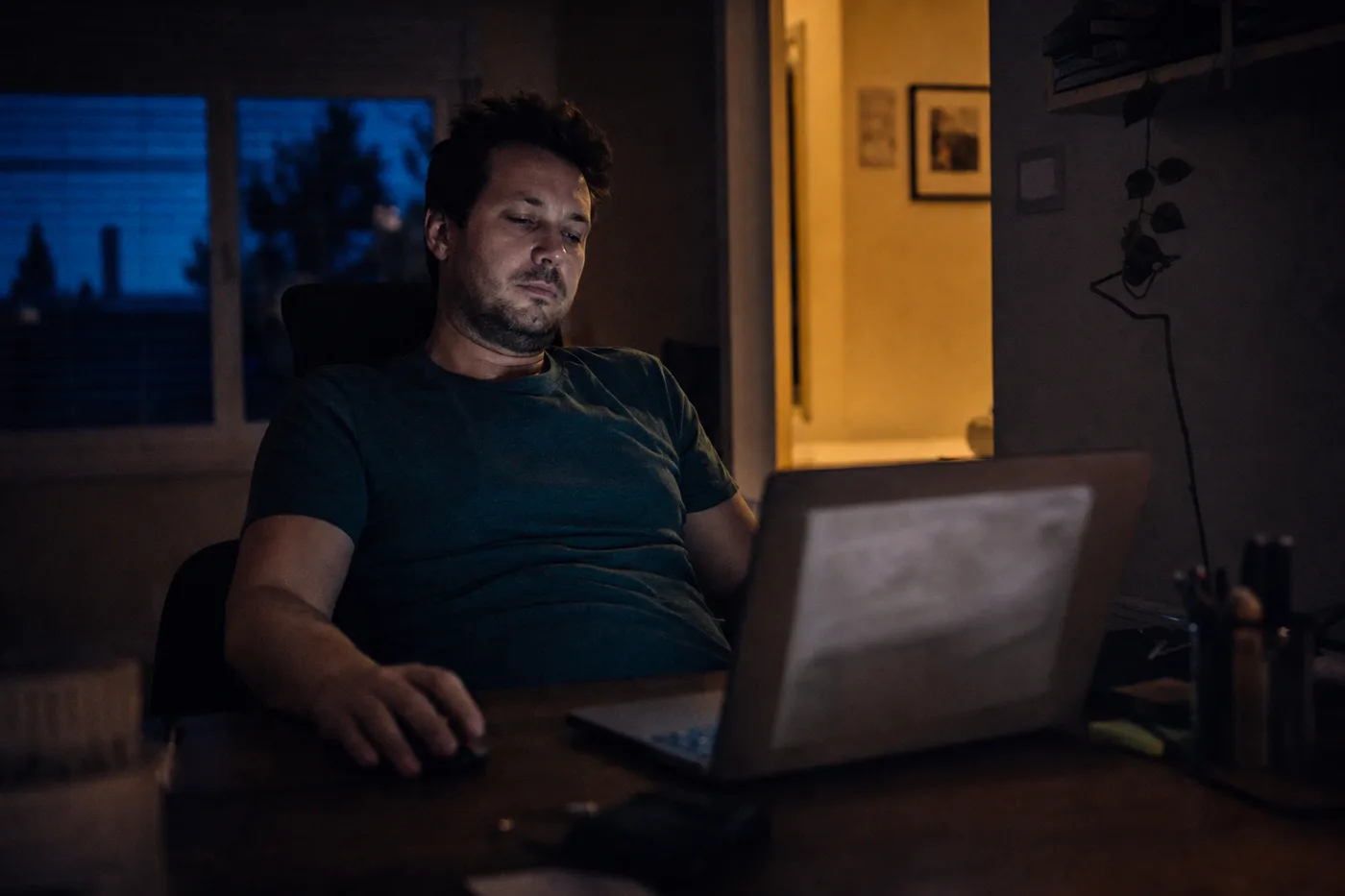 A learner passively accepting an AI tutor's answer at his laptop without checking it, lit by screen glow