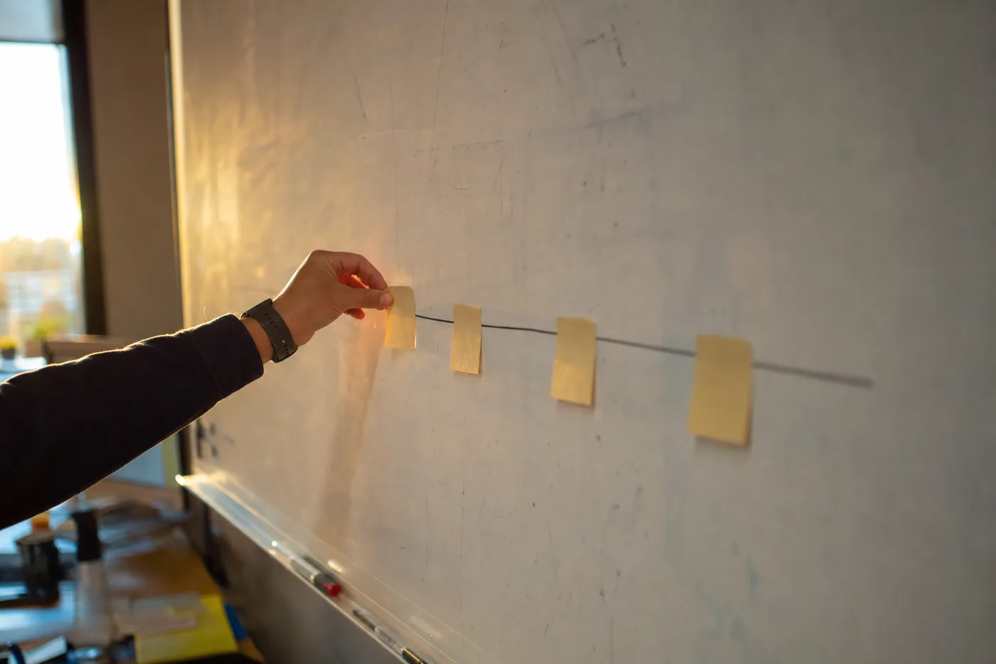 A hand placing sticky notes at regular intervals along a whiteboard line, showing checkpoints spaced through a lesson