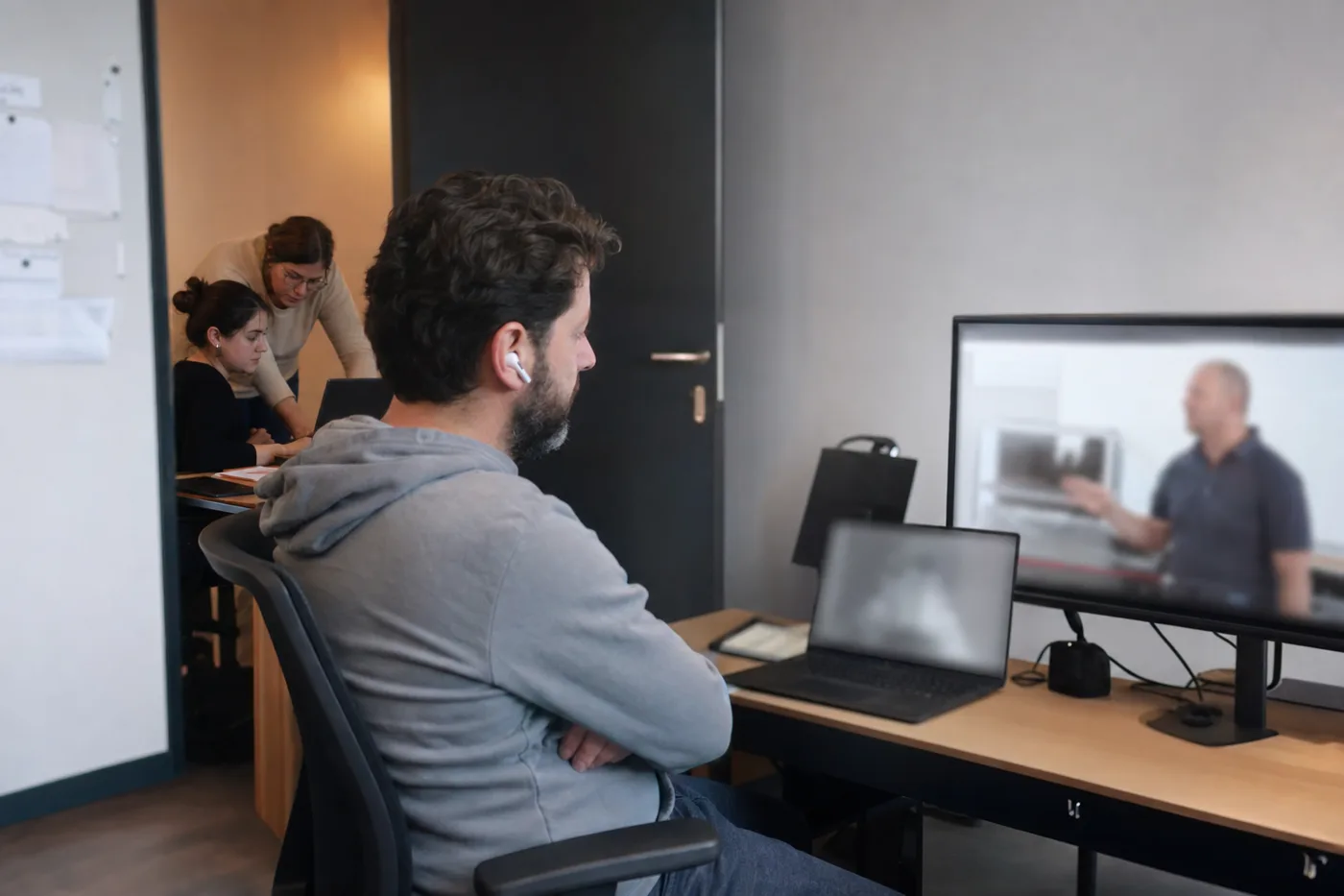 A disengaged employee watching a training video in front, while two colleagues behind practice a task hands-on together