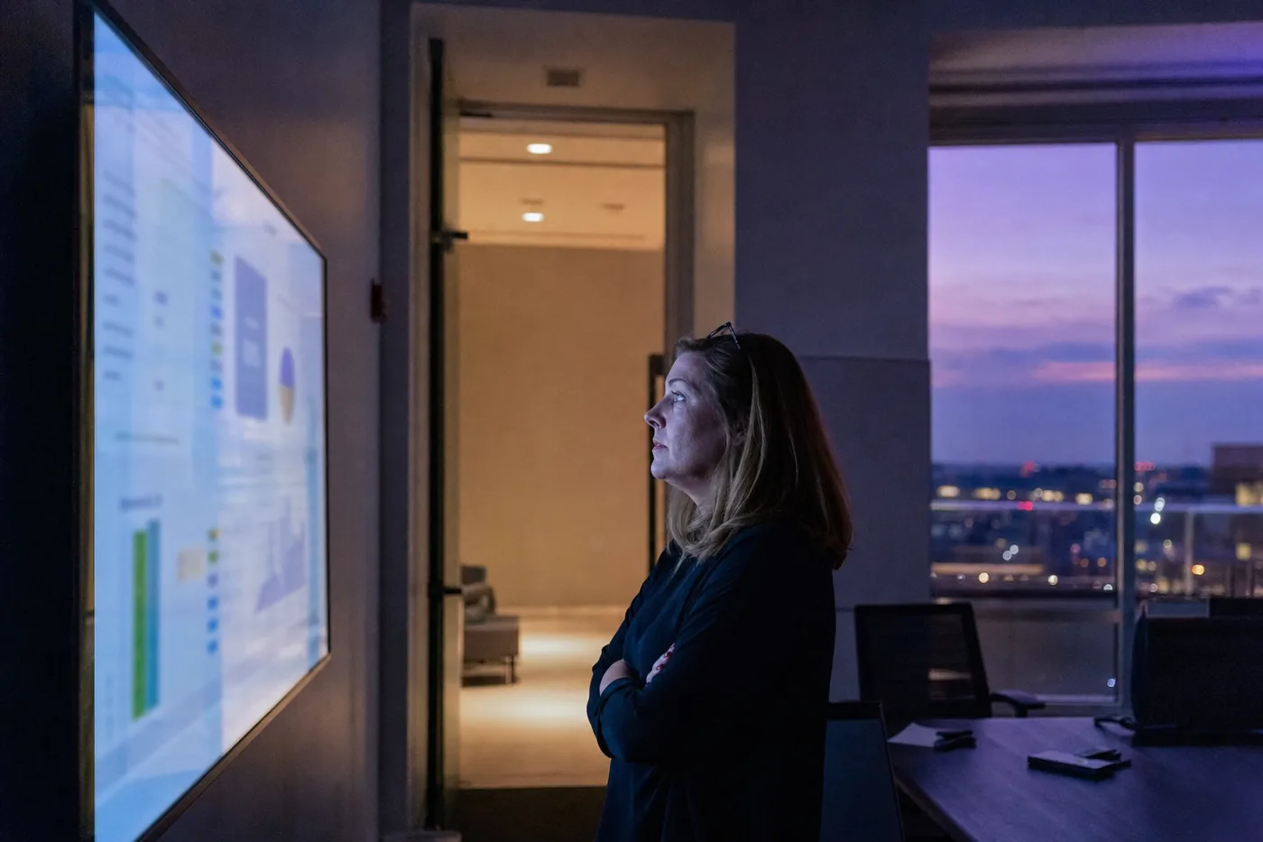 An L&D director studying blurred training dashboards on a wall screen at dusk, weighing how to close the AI skills gap