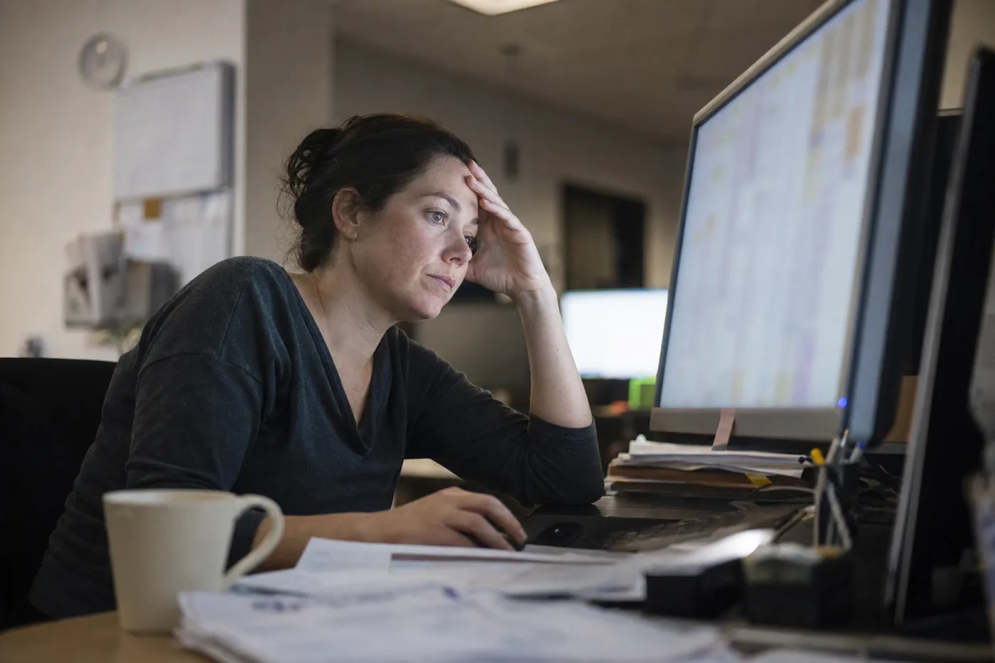 An overwhelmed employee at her desk facing a dense wall of on-screen content, a picture of cognitive overload in training