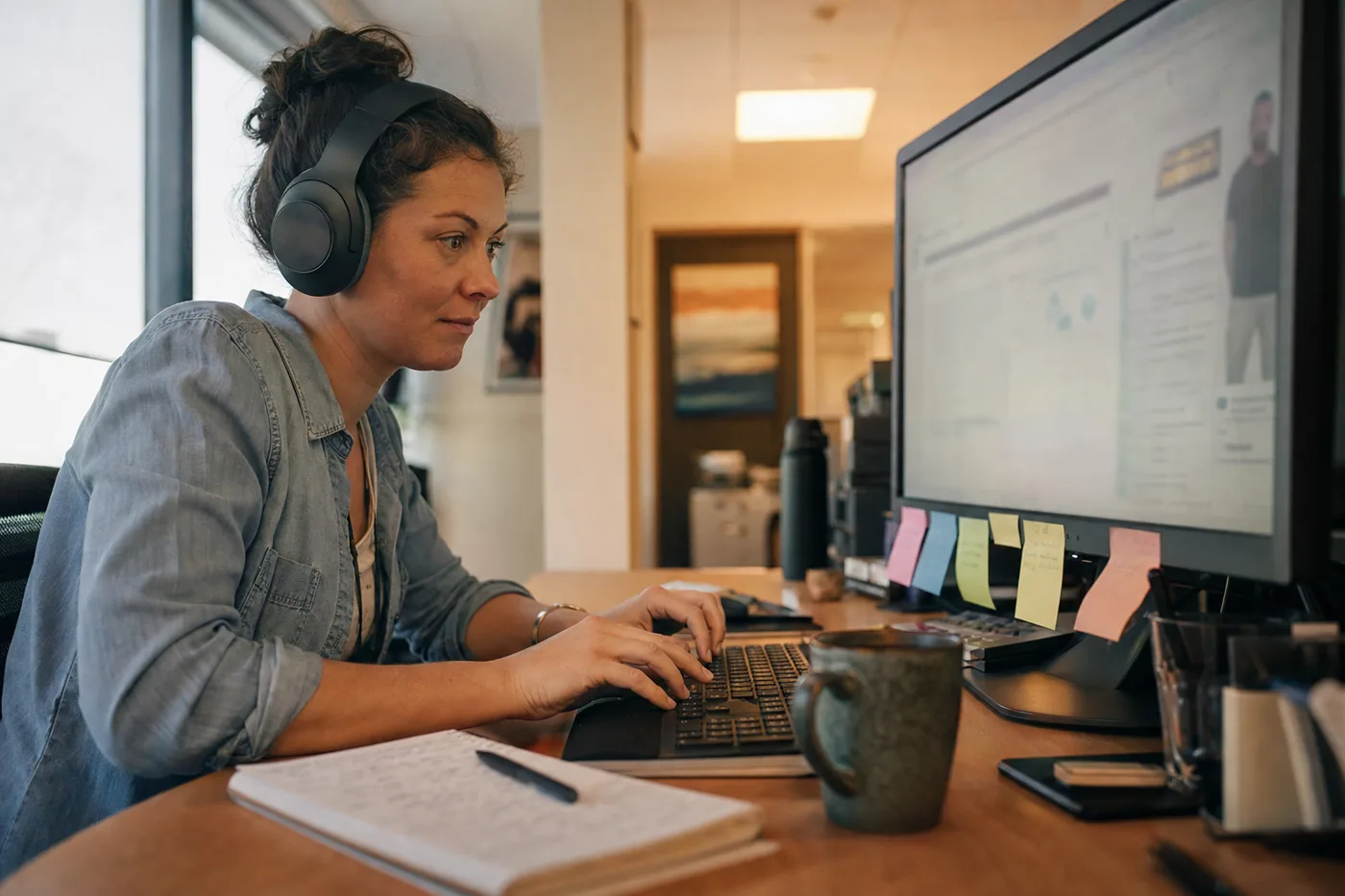 A learner in headphones actively typing a response during a lesson with an AI tutor at her office desk