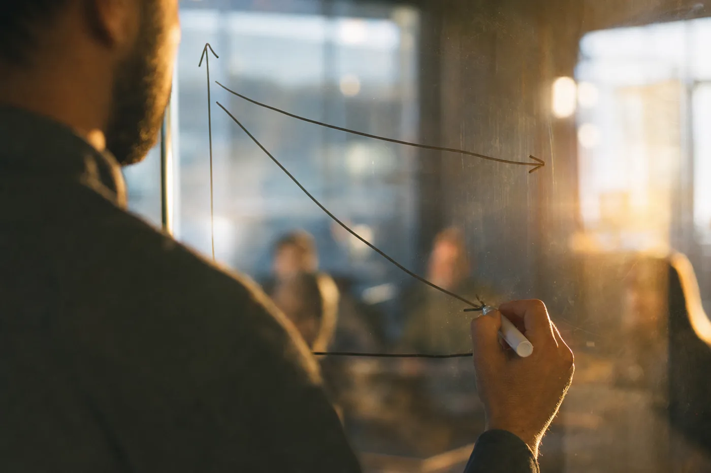 A hand drawing the steep employee training retention forgetting curve on a glass wall, with a second flatter curve above it