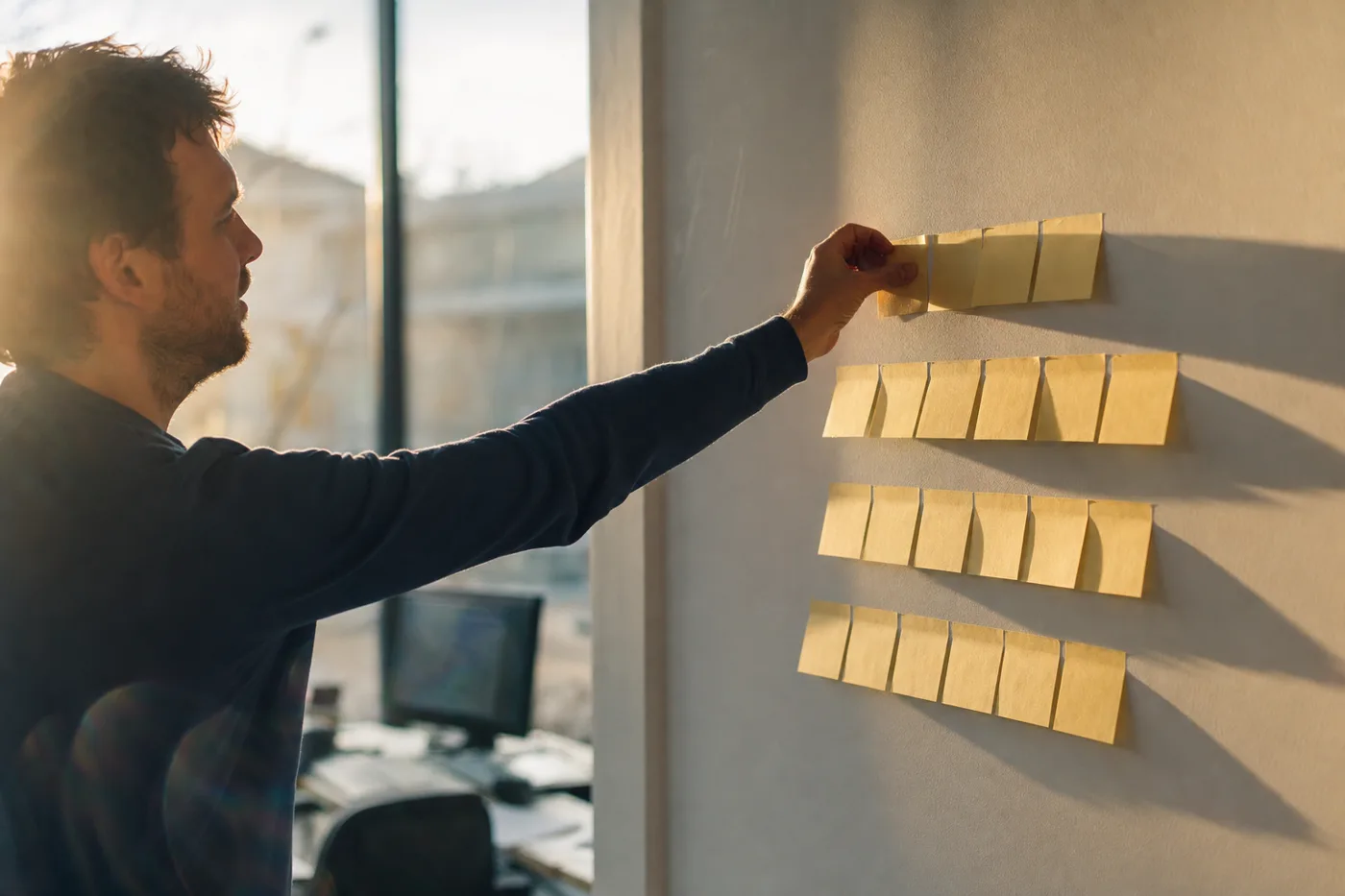 A hand pressing the top note onto four ascending rows of sticky notes, laying out the four levels of training measurement