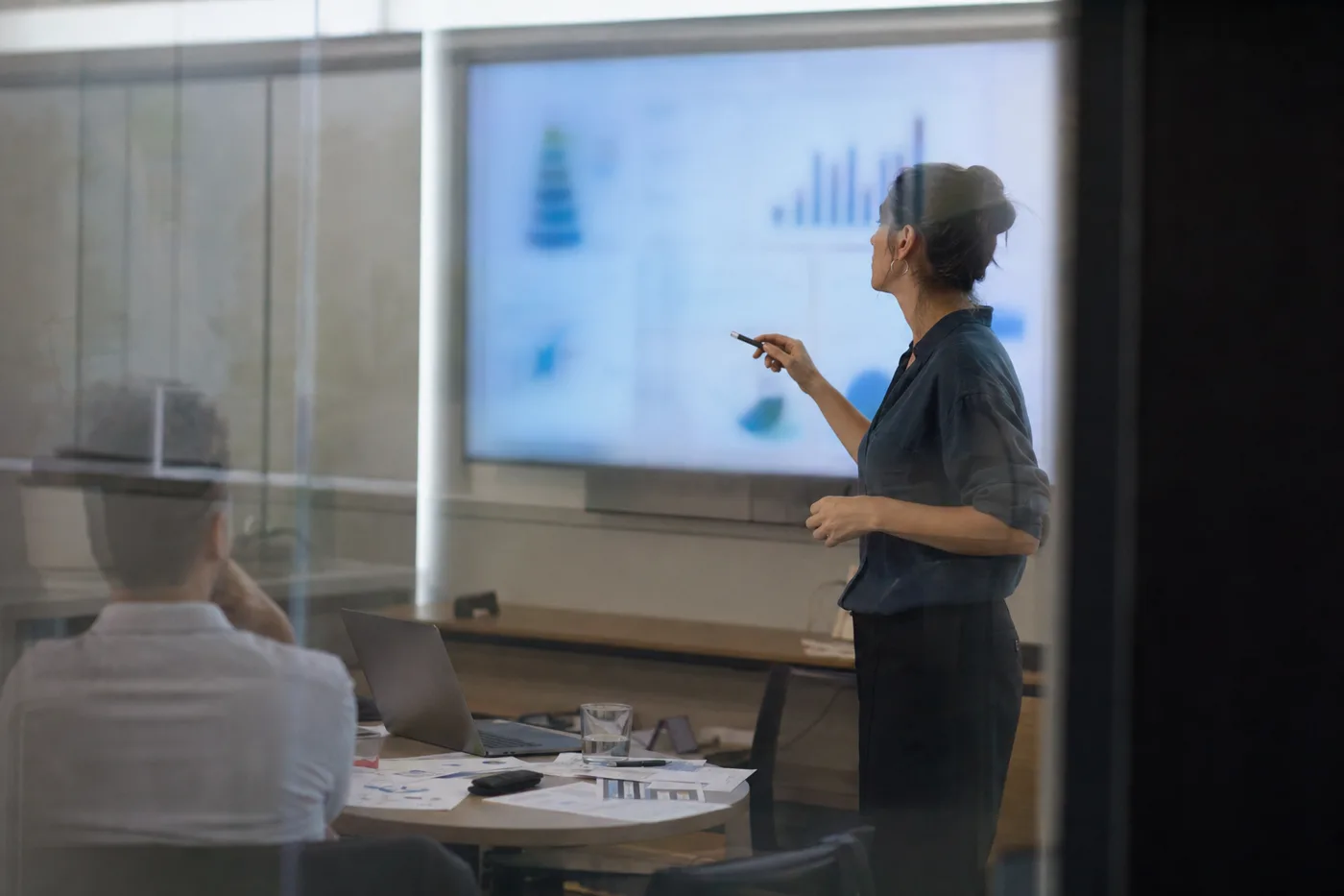 An analyst studying blurred training charts on a meeting room wall screen, measuring training effectiveness beyond completions