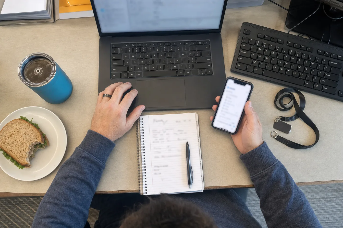 An overhead view of a desk with a laptop, phone, and notebook competing for one person's attention