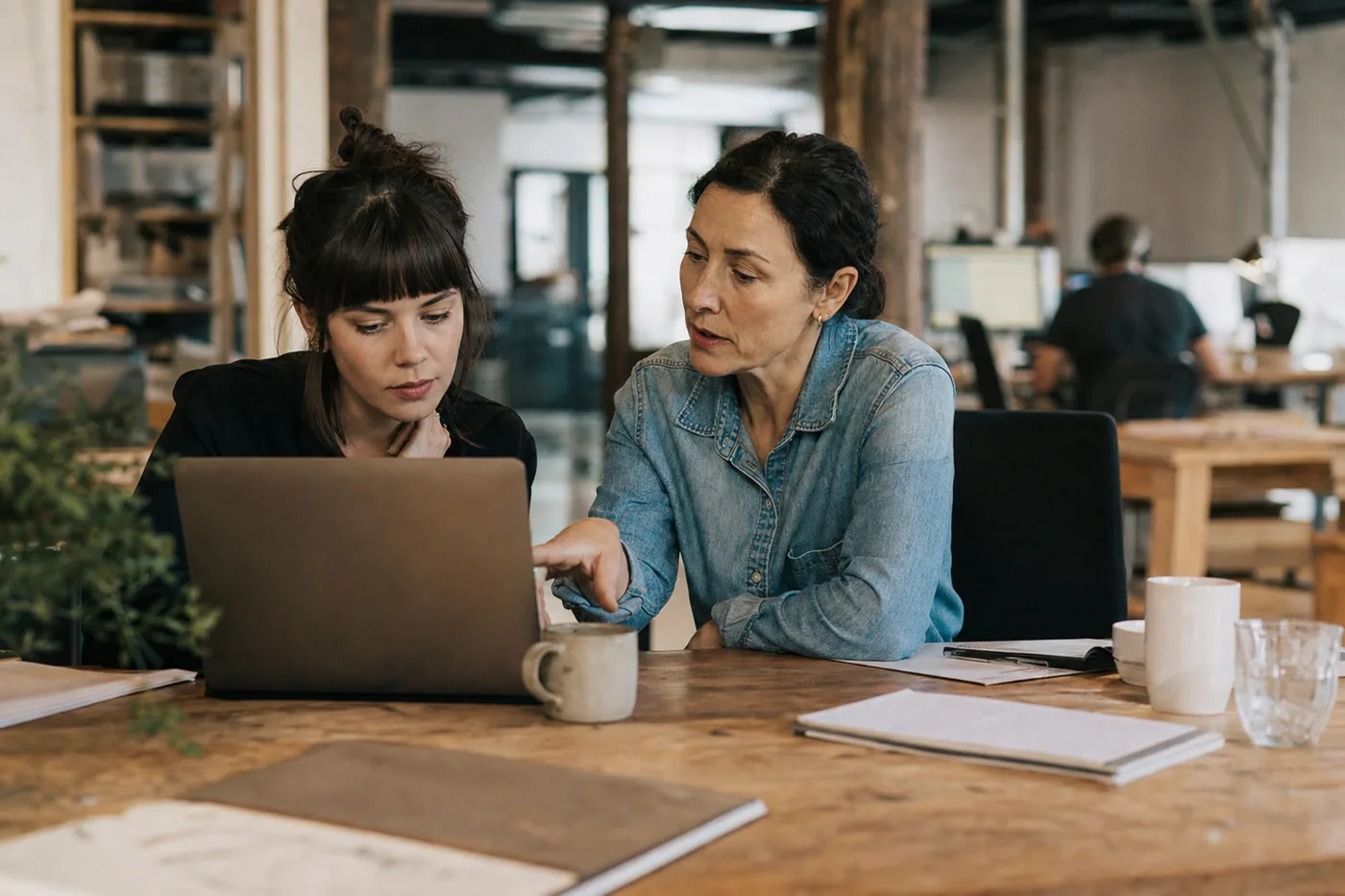 A new hire pairing with a colleague at a desk to ramp up, illustrating new-hire time to productivity