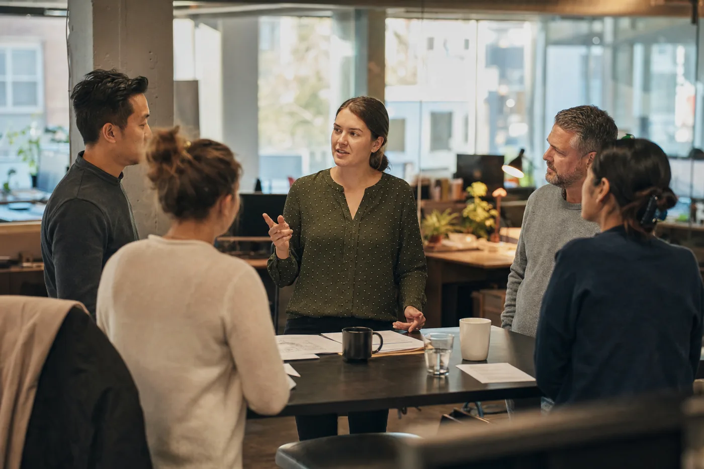 A newly promoted team lead runs a morning huddle during new manager training in a bright open office