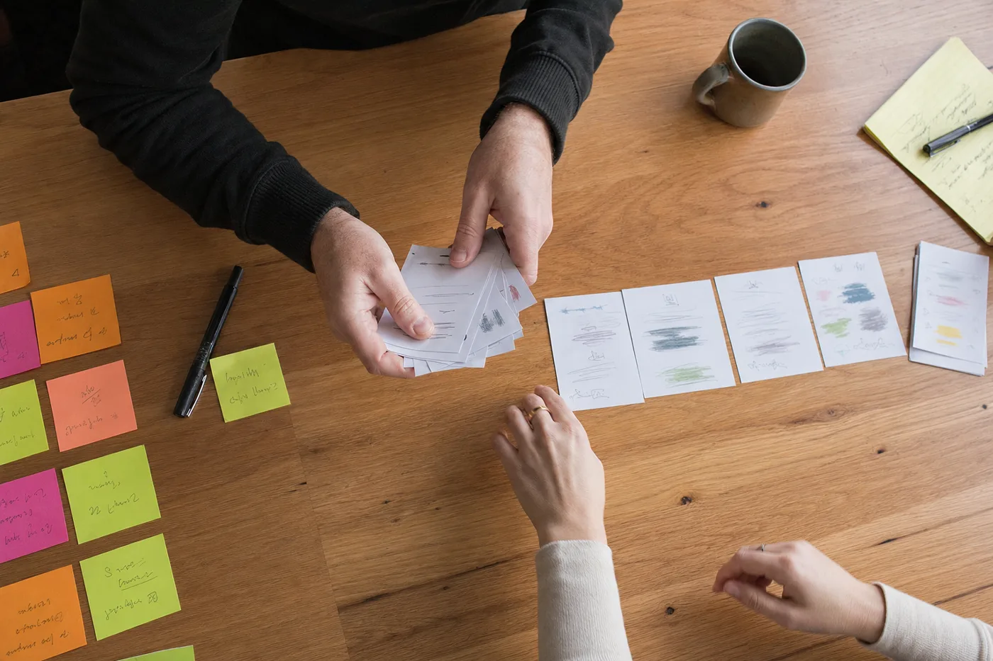 Hands arrange printed program cards into a shorter row on a desk, planning a compressed new manager training timeline