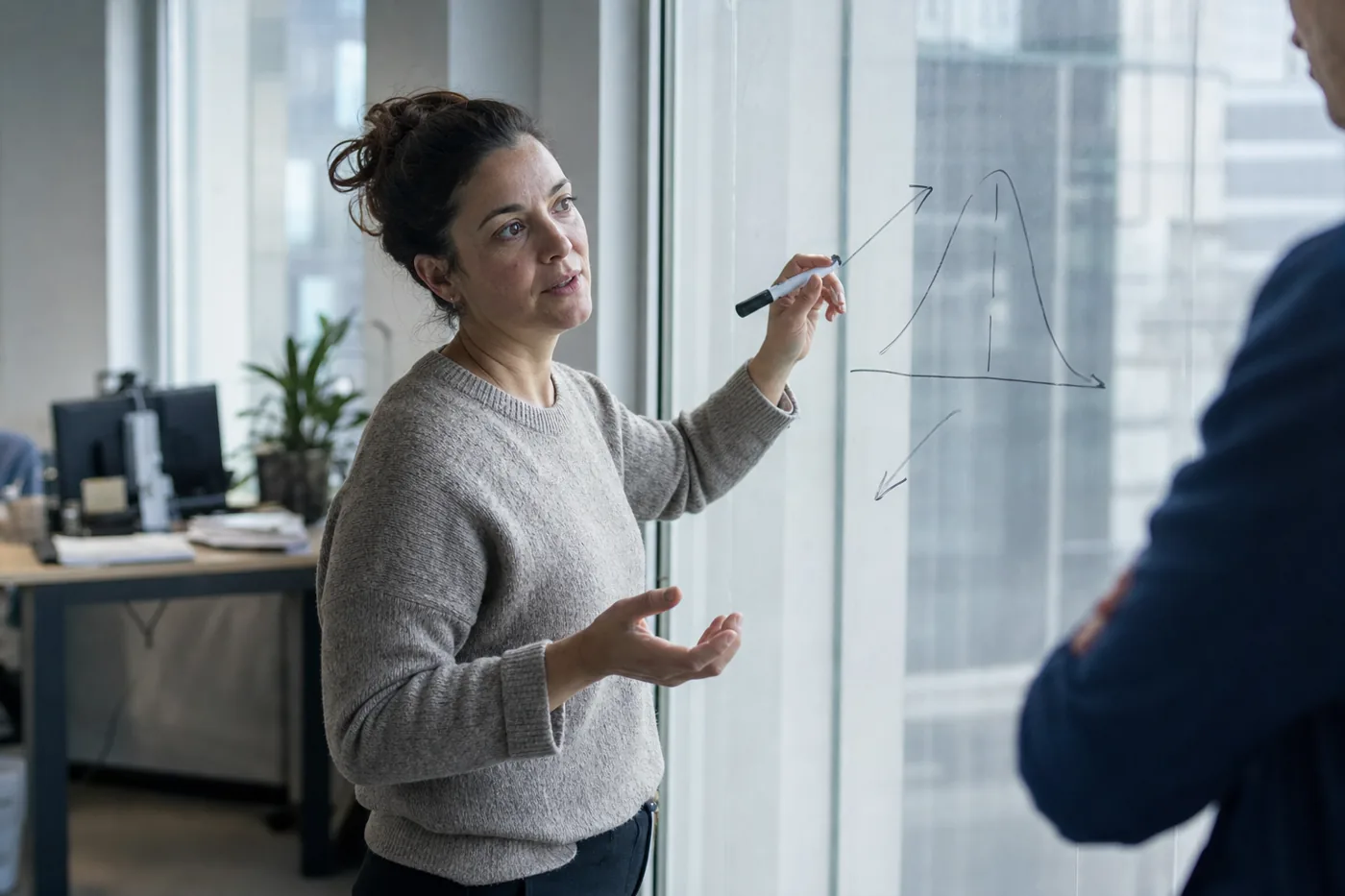A coworker sketching a rough performance curve on a glass wall while explaining it to a colleague