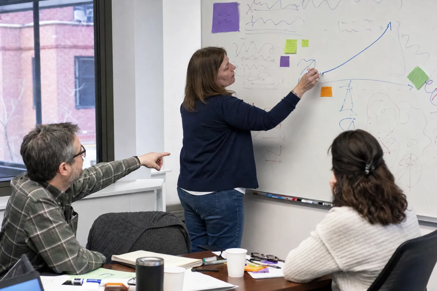Trainer sketching a rising performance curve on a whiteboard during a practice-based workshop