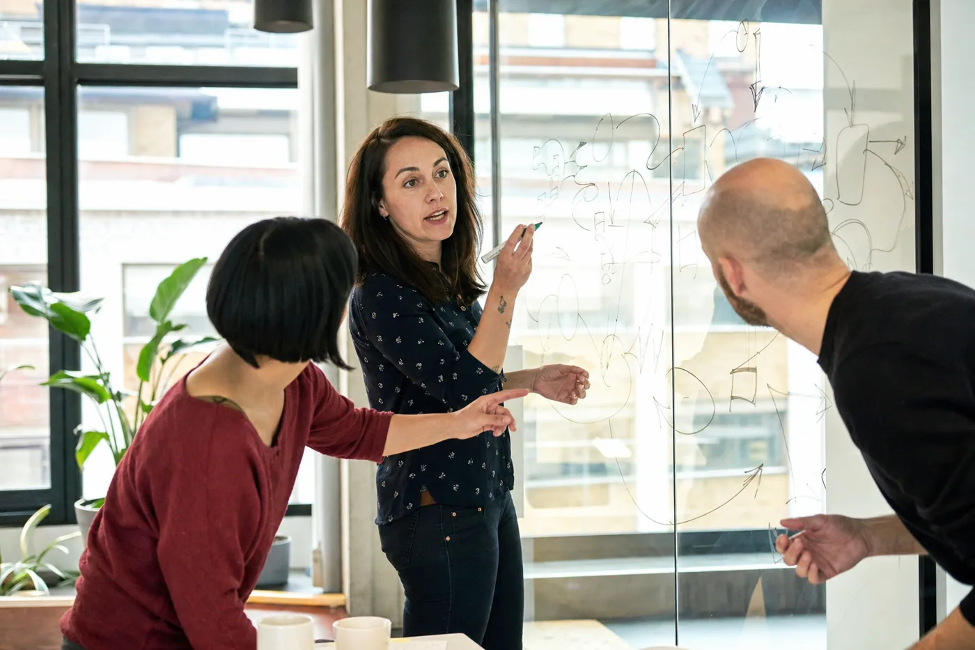 Coworkers using retrieval practice and active recall in a training session, explaining ideas at a glass wall
