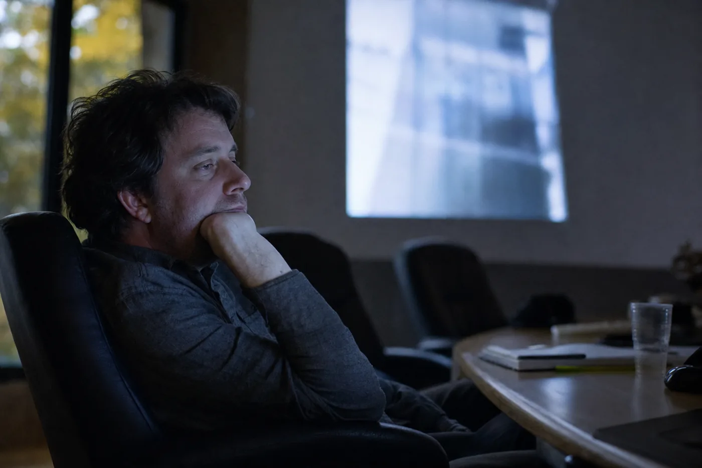 A disengaged employee slumped in a dim conference room half-watching an out-of-focus projected slide in the late afternoon