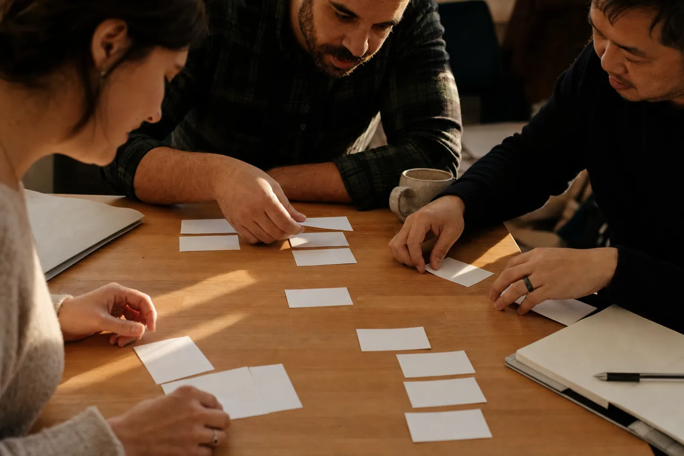 A manager and two team members arranging printed skill cards into personalized clusters on a wooden desk in warm afternoon light