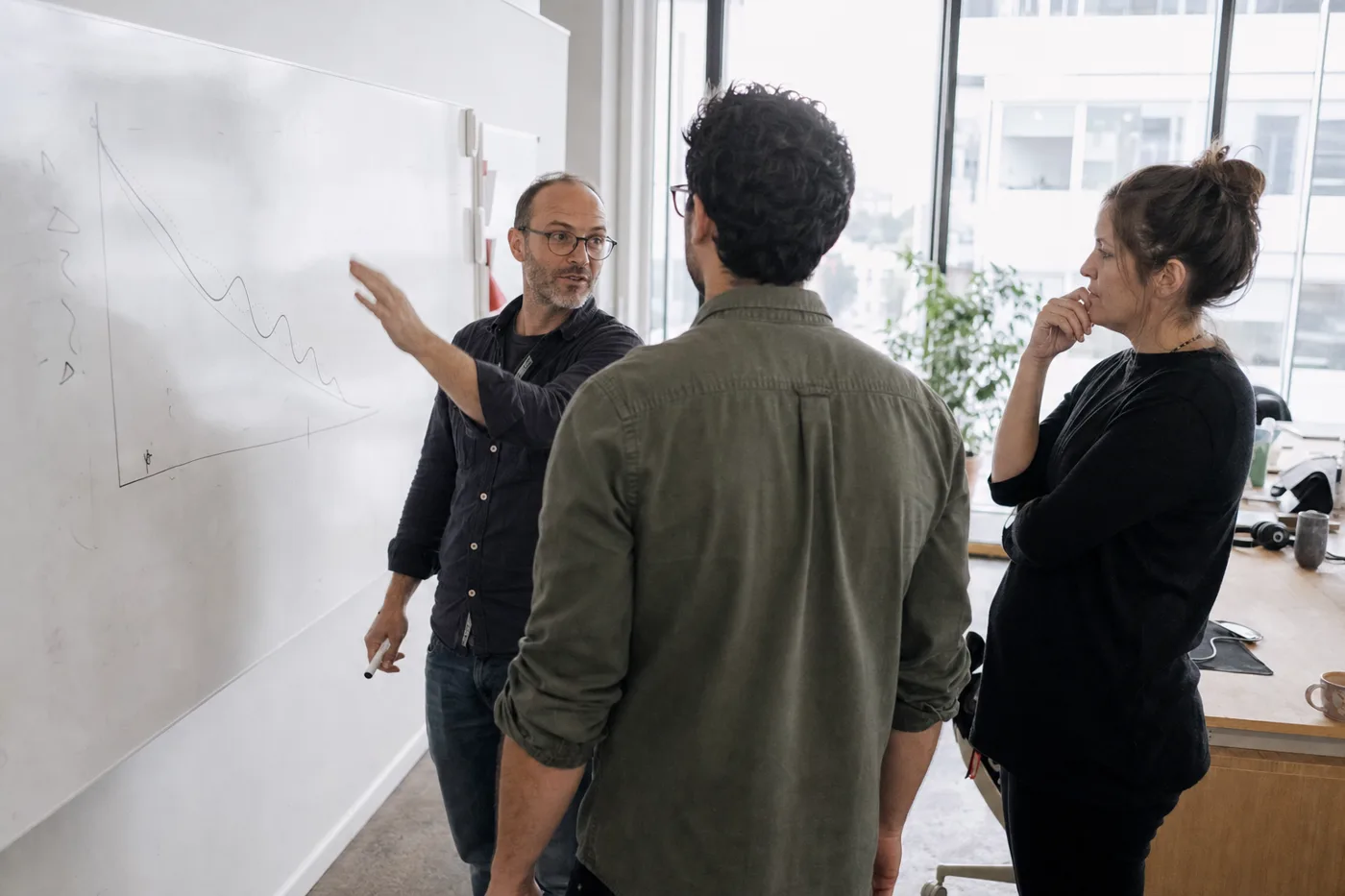Coworkers mapping a forgetting curve on a whiteboard during a spaced repetition training session in a bright office