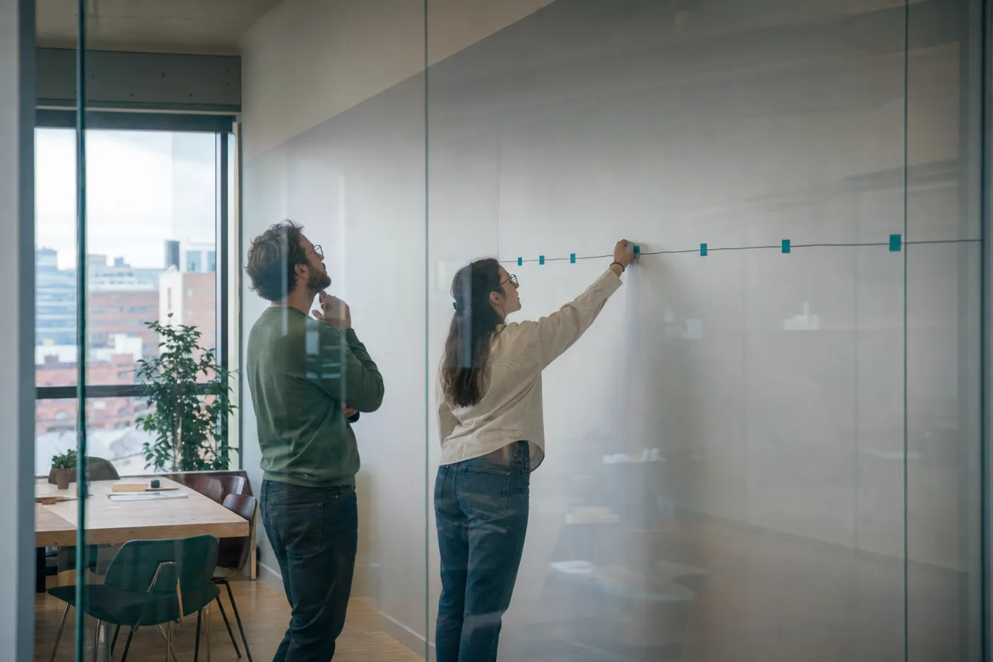 Two coworkers marking spaced review intervals along a line on a wall, building distributed practice into a training schedule